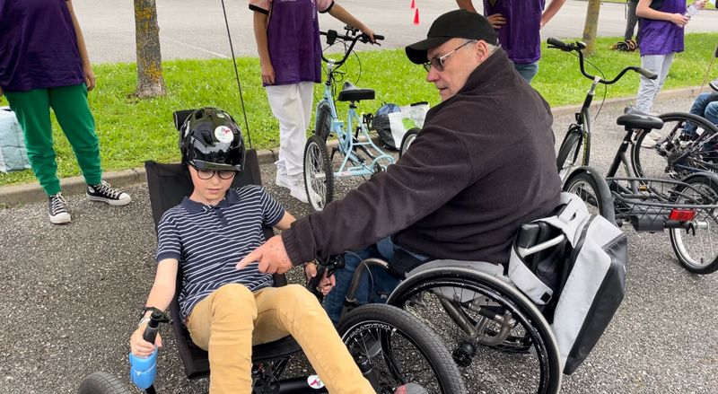 Un homme en fauteuil roulant conseillant un jeune garçon essayant un tricycle allongé 