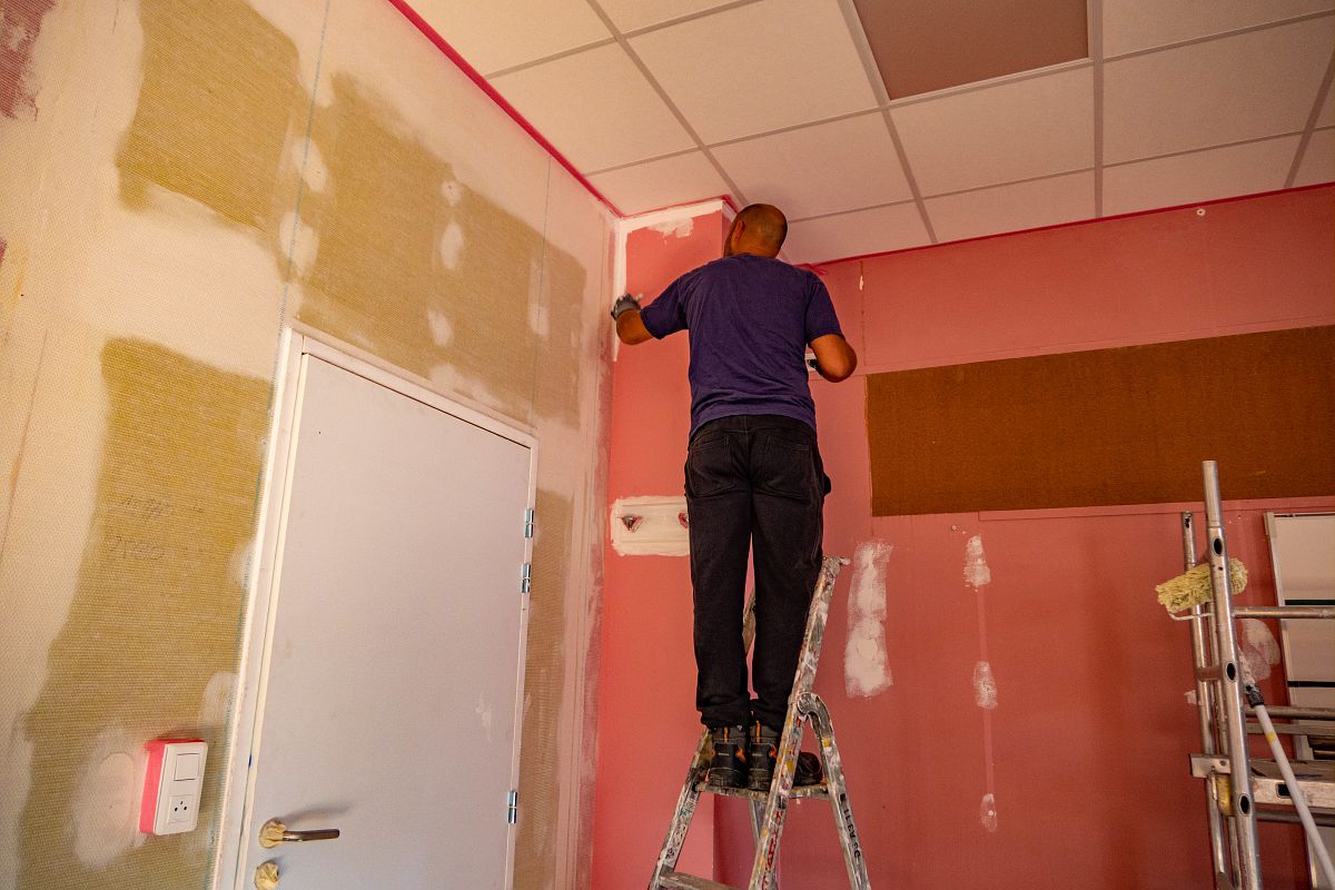 Une personne sur un escabeau fait des travaux dans sa maison